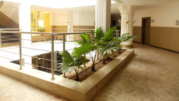 Un lobby espacioso con piso de mármol, un jardín vertical en el centro y una escalera que conduce a un nivel superior.