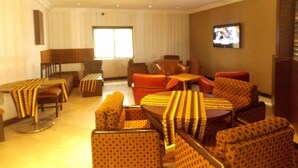 Un hall de hotel con diversas opciones de asientos, incluyendo sofás y sillones, un televisor montado en la pared y un amplio ventanal que proporciona luz natural.