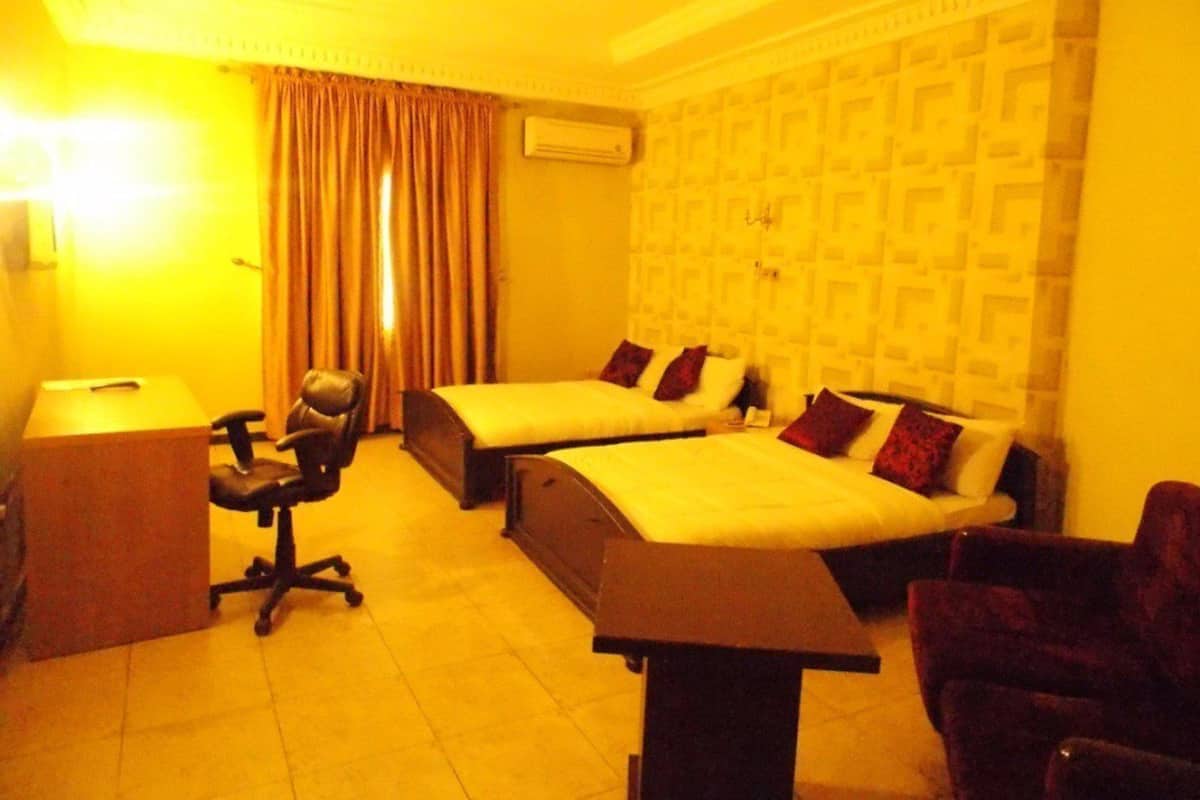 A hotel room with two beds, a desk, a chair, and an air conditioning unit.