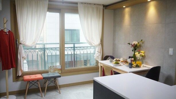 A modern kitchen with a dining table, a window with curtains, and a balcony view. - Lee & No Guesthouse (Seoul)