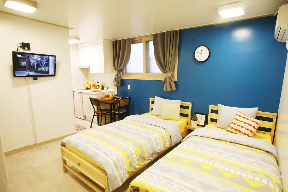 Una camera da letto con due letti, una scrivania, una sedia, una televisione e una sveglia appesa al muro.