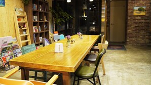 A wooden table with chairs, surrounded by bookshelves and a plant. - Lee & No Guesthouse (Seoul)
