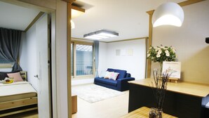 A modern hotel room with a bed, a blue sofa, a wooden table, and a vase of flowers. - Lee & No Guesthouse (Seoul)