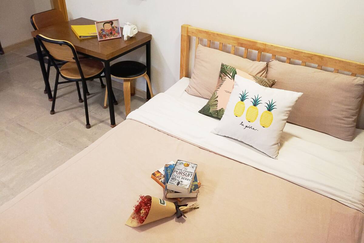 Una camera da letto con un letto di legno, un tavolino con sedie e un comodino con un libro e un oggetto decorativo.
