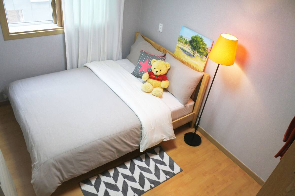 Un letto rifatto con un copriletto bianco e un orsacchiotto sull'alletto.