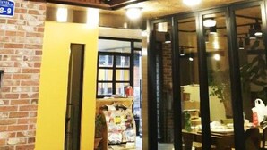 A building with a brick facade, a yellow door, and a glass entrance leading to an interior space with tables and chairs. - Lee & No Guesthouse (Seoul)