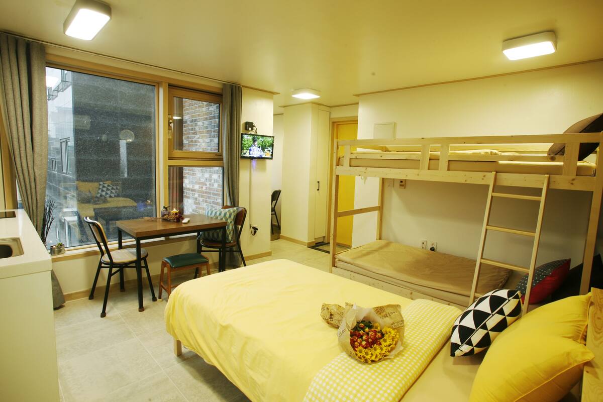 Una camera d'albergo con un letto a castello, una scrivania con una sedia, una televisione e una finestra con tende.