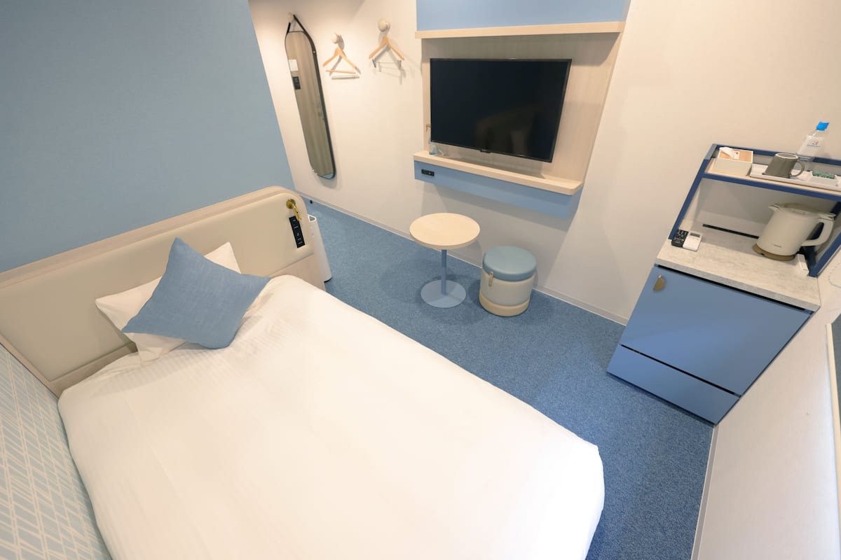 Une chambre d’hôtel avec un lit, une petite table ronde, une télévision, un miroir et un bureau avec une bouilloire.