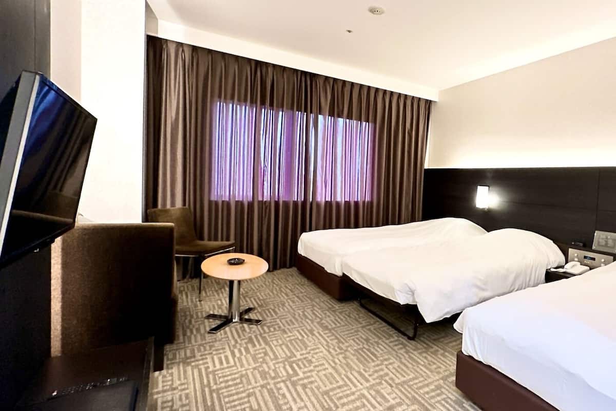 Une chambre d’hôtel avec un lit, un bureau, une chaise, une télévision et une fenêtre avec des rideaux.