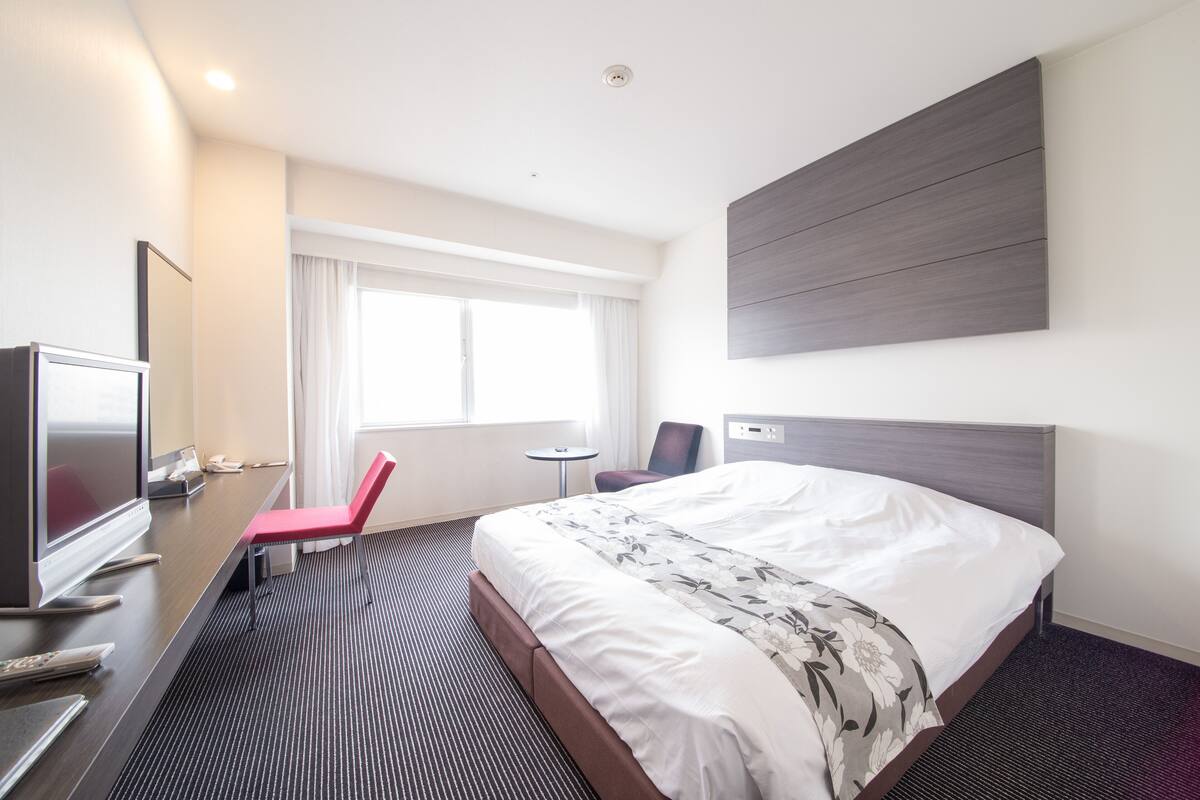 Une chambre d’hôtel avec un grand lit, un bureau avec une télévision, une chaise et une petite table.