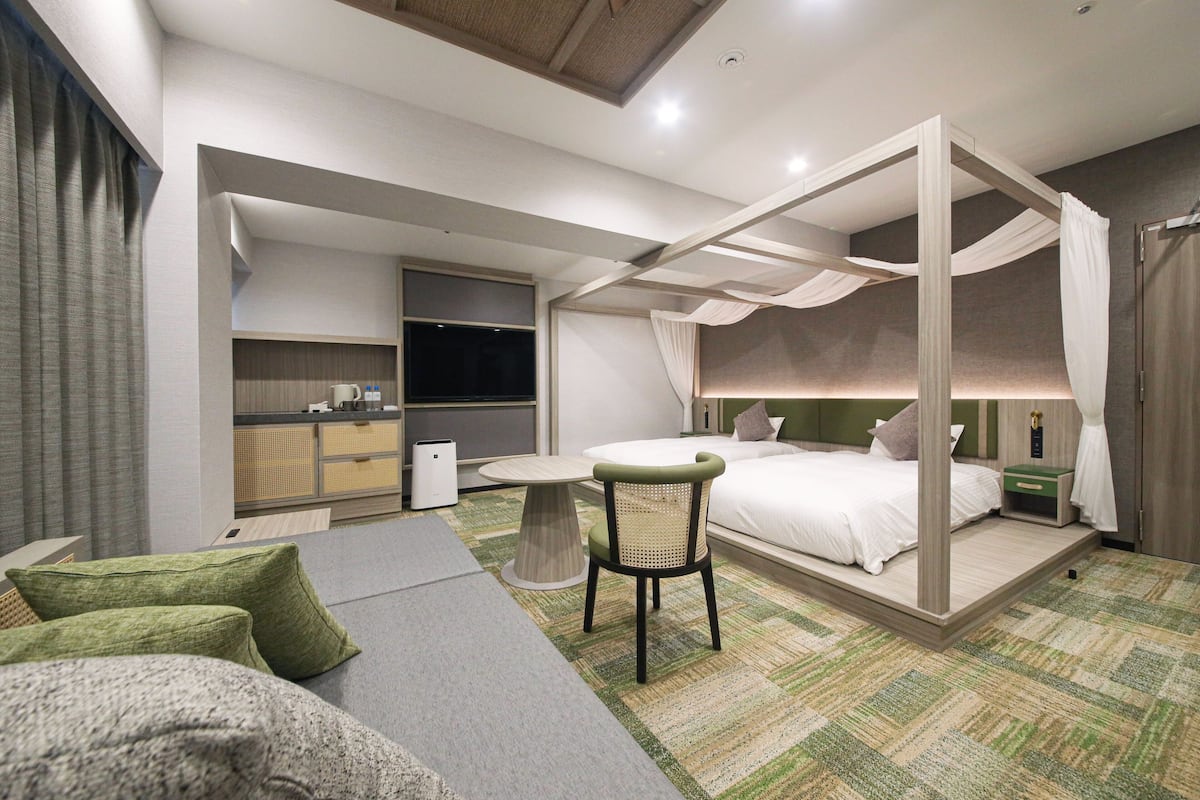 Une chambre d’hôtel moderne avec un lit à baldaquin, une petite table à manger, un canapé confortable et un téléviseur.