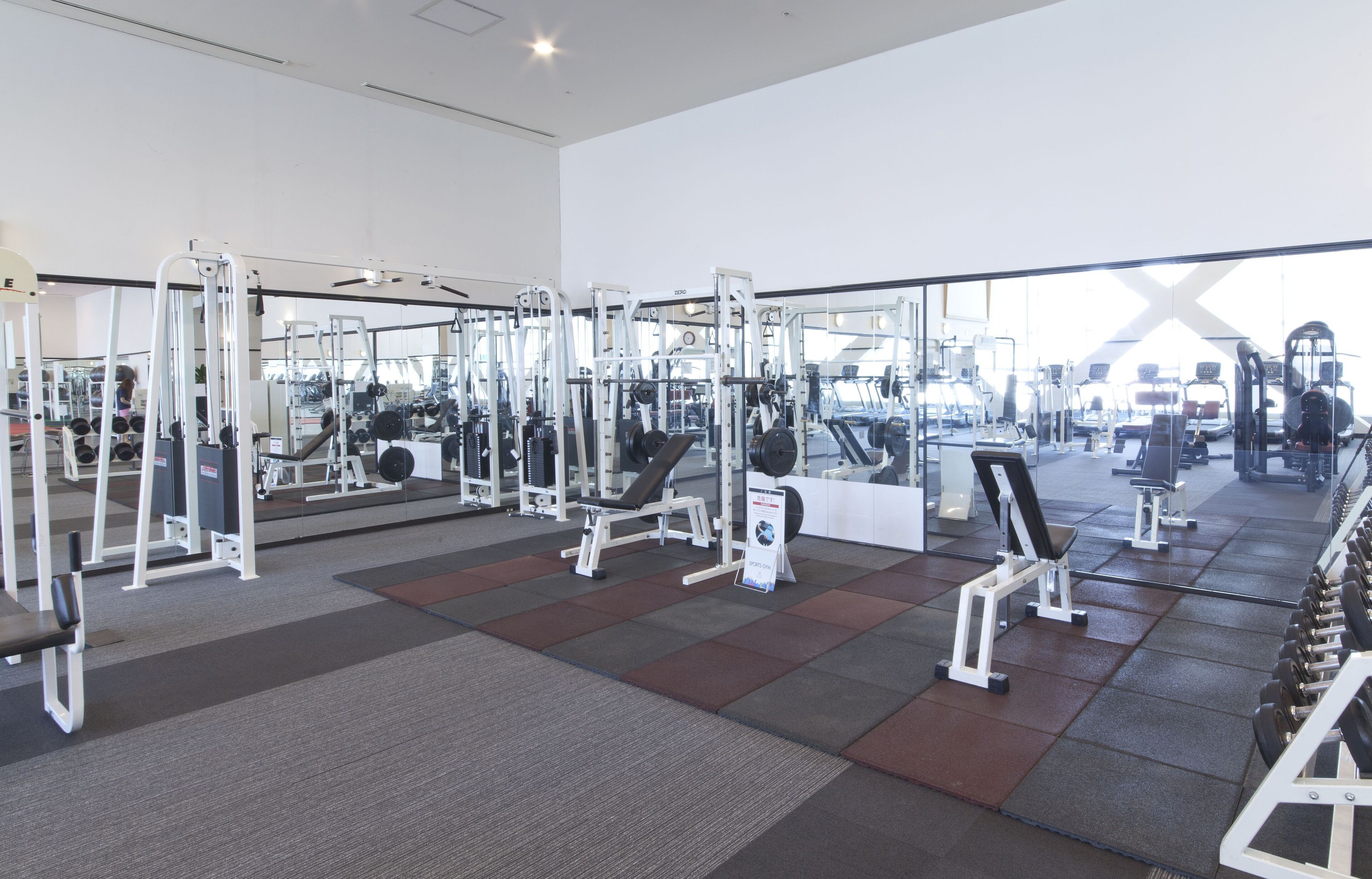 Un gimnasio con diversas máquinas de ejercicio, un muro de espejos y piso de baldosas.