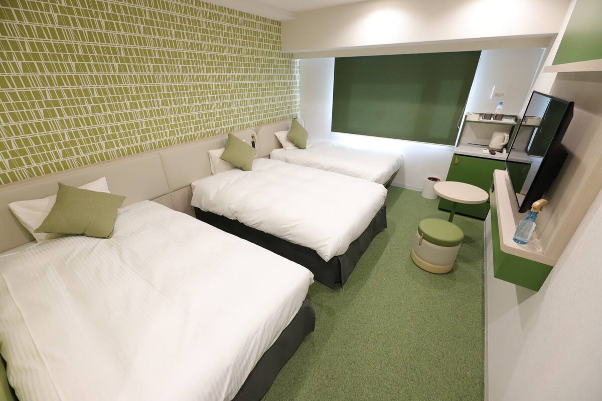 Une chambre d’hôtel avec deux lits, une petite table, un mur d’accent vert et un téléviseur.