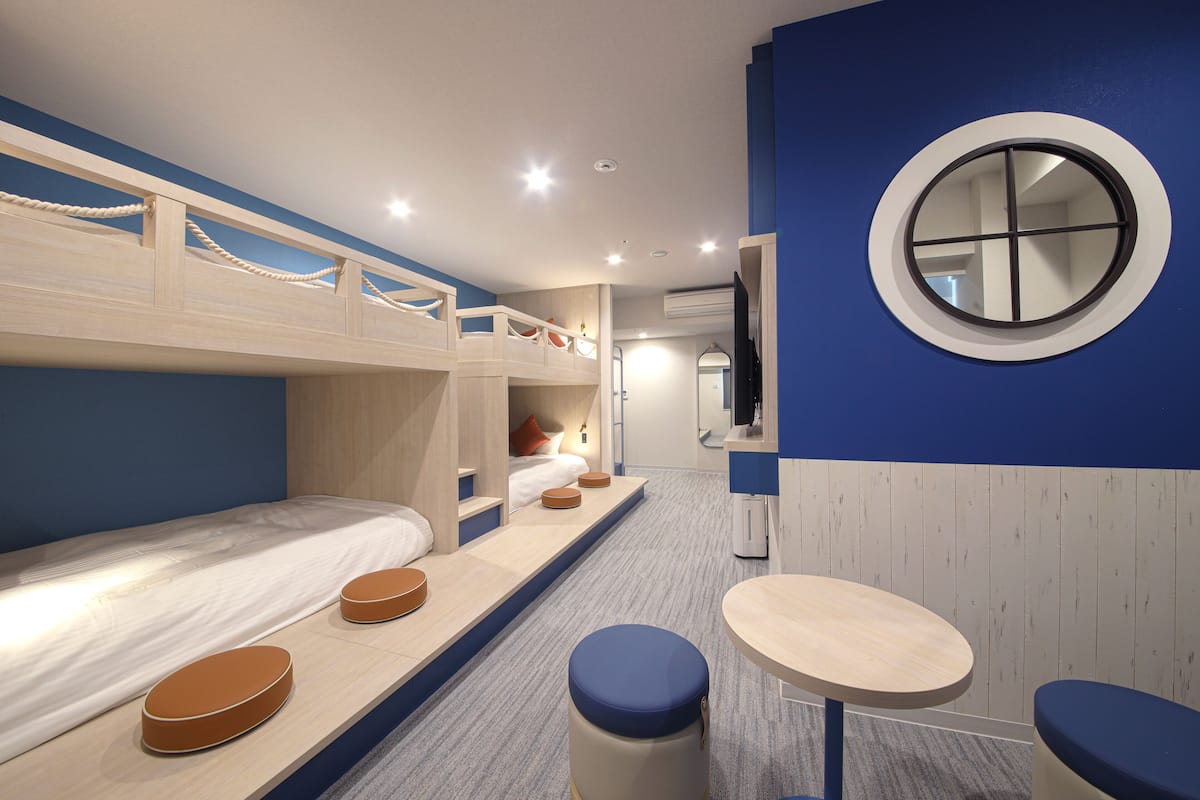 Une chambre avec un lit superposé, un petit miroir rond, une petite table et un coin salon.