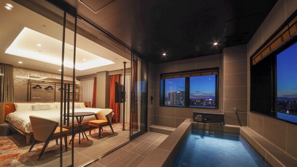 A modern hotel room with a glass-enclosed bathroom, a private balcony with a view of the cityscape, and a small pool area. - Spa World (Osaka)