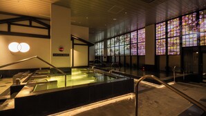 A modern indoor pool area with clear glass walls, a visible clock, and a sign indicating the pool's temperature. - Spa World (Osaka)