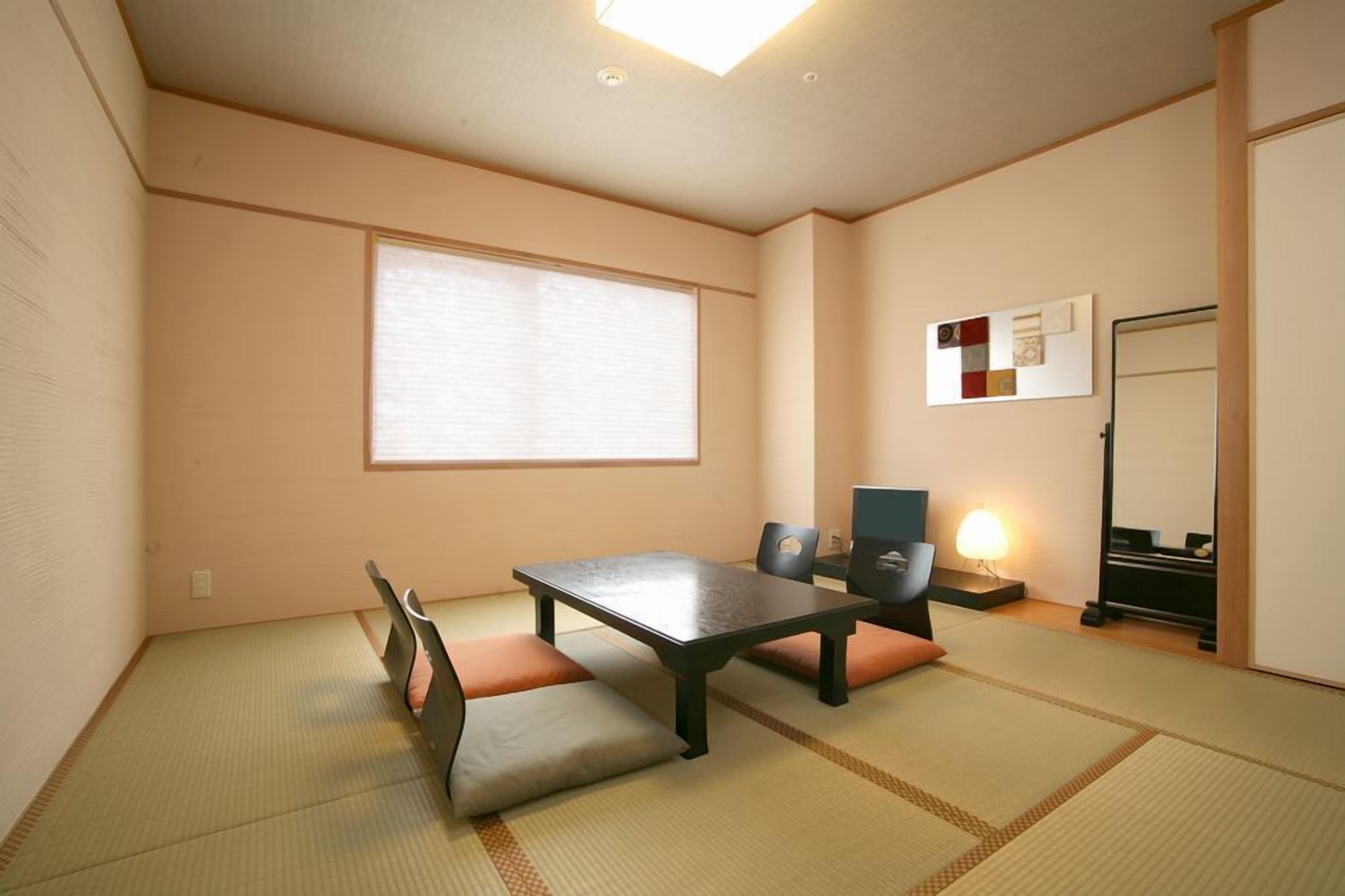 A traditional Japanese room with tatami flooring, a low table, cushions, a sliding door, and a wall-mounted shelf.