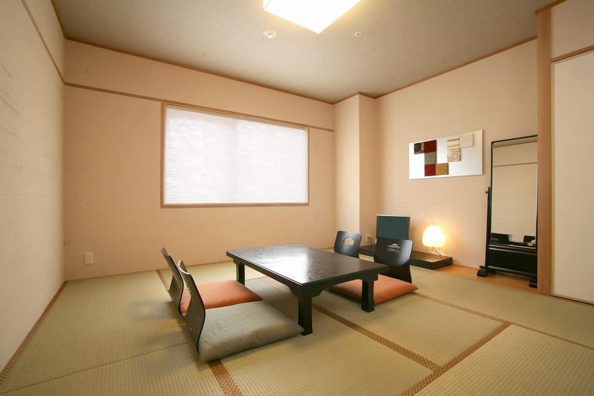 Une pièce de style japonais traditionnel, avec un sol recouvert de tatamis, une table basse, des coussins, une porte coulissante et une étagère fixée au mur.