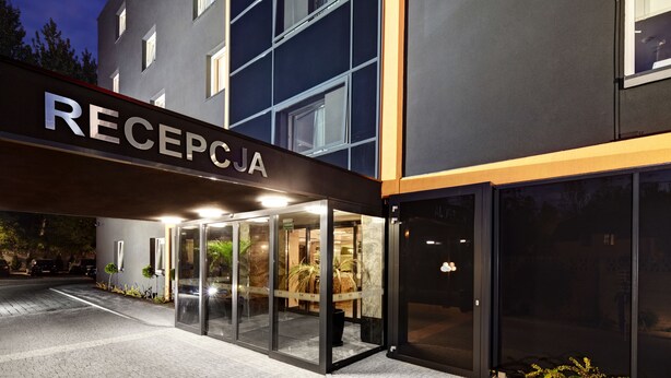 A modern hotel entrance with a reception desk, glass doors, and a sign reading "RECEPTION". - M Hotel Sosnowiec (Sosnowiec)