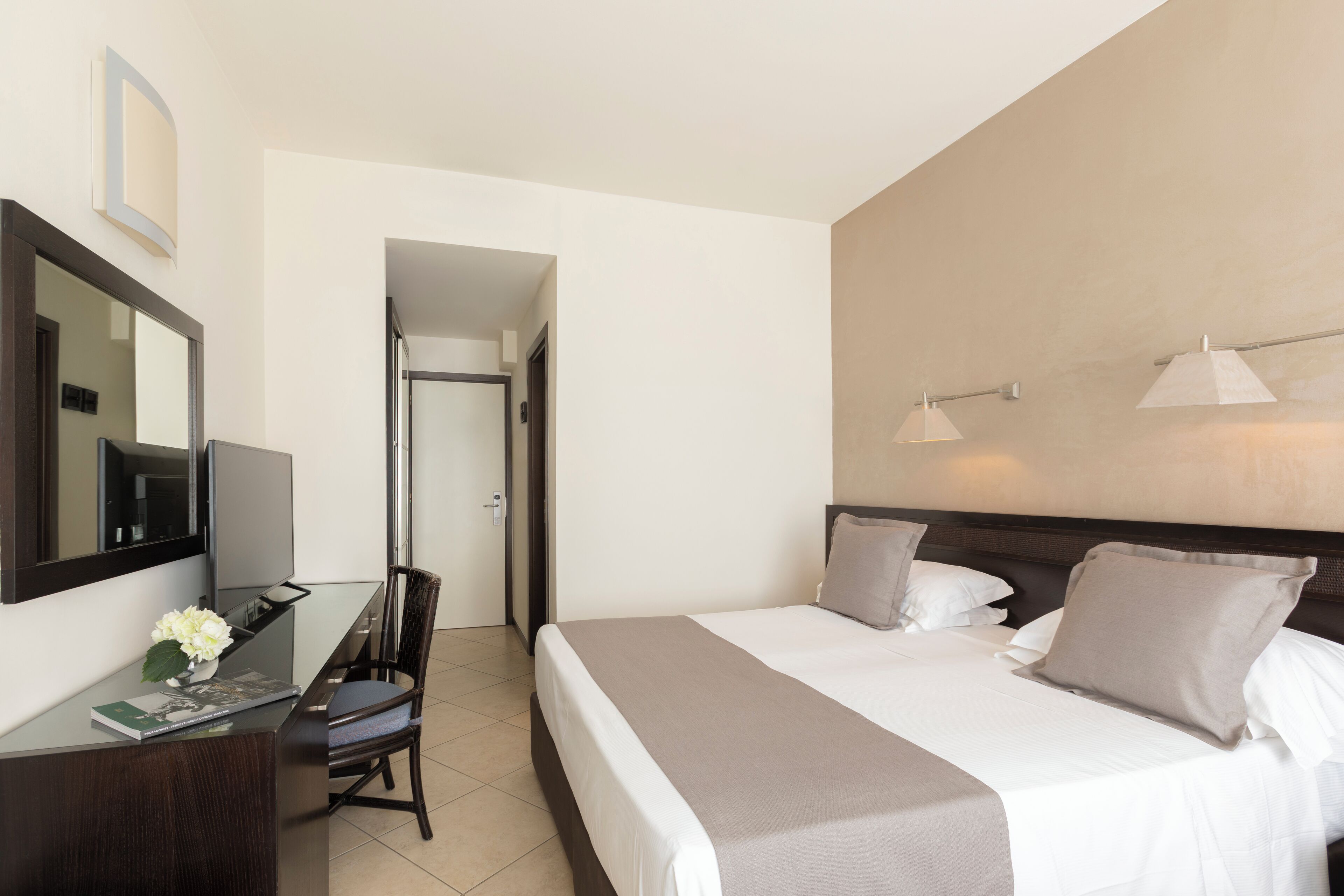 Una habitación de hotel con cama, escritorio, silla, espejo y puerta que da a otra habitación.