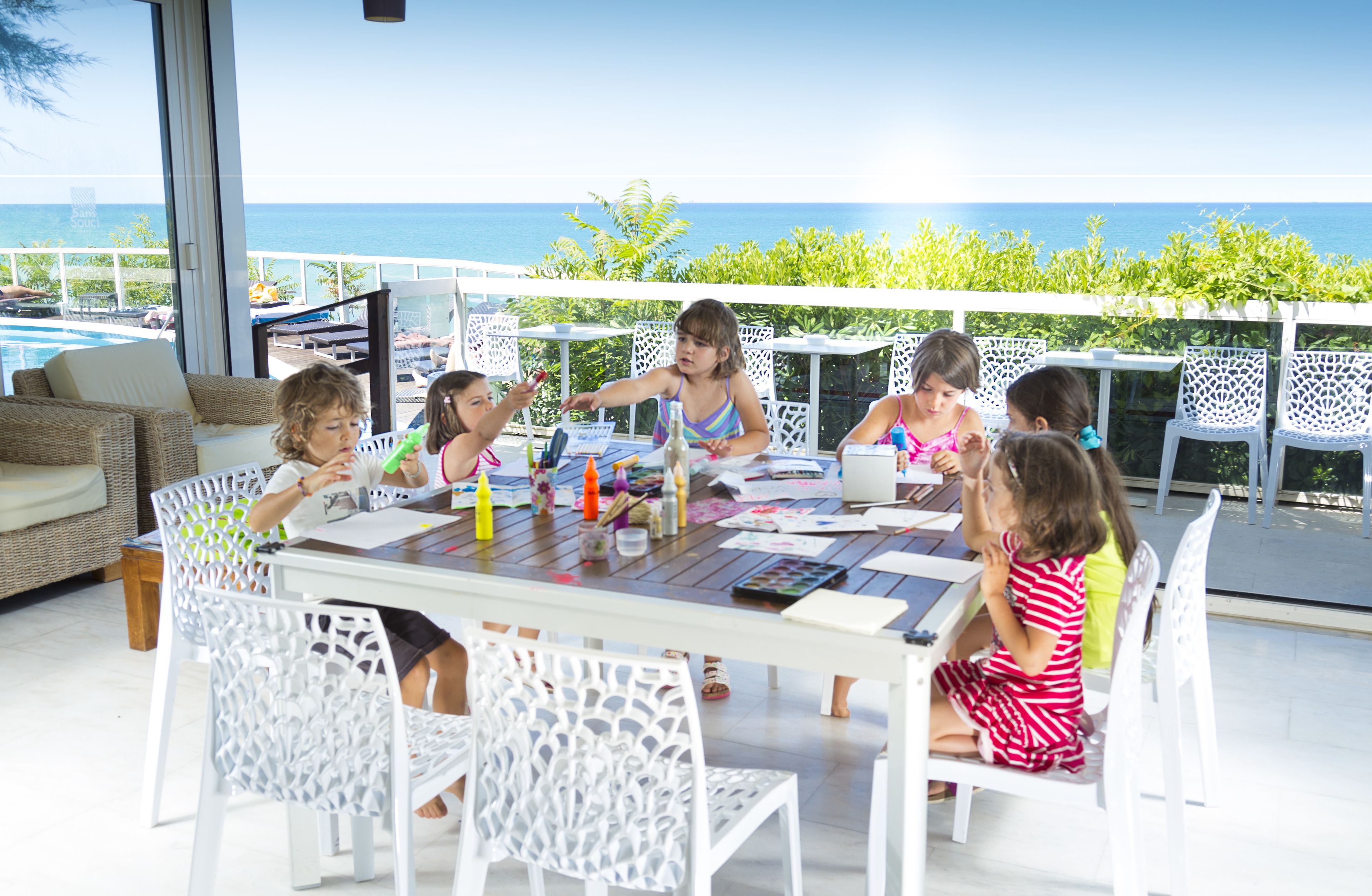 A group of children engaged in an art activity at a table with a view of the ocean.