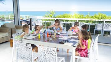 A group of children engaged in an art activity at a table with a view of the ocean.
