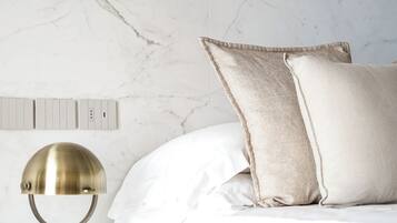 Una cama bien hecha con ropa blanca, una lámpara de escritorio de latón y una mesita de noche de madera.