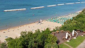 A beach with a wooden deck area featuring outdoor seating and umbrellas. - Hotel Sans Souci (Gabicce Mare)
