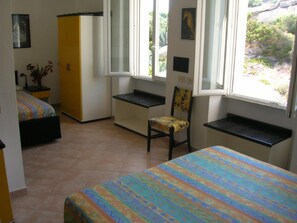 Ein Schlafzimmer mit Bett, Stuhl, Schreibtisch und einem Fenster mit Blick auf Grünflächen.