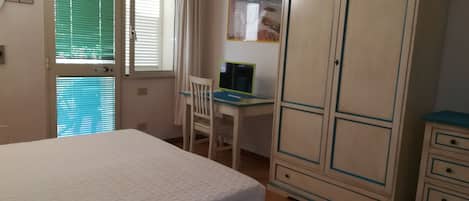 A bedroom with a bed, a desk with a computer, a wardrobe, and a window with blinds.