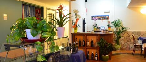 A hotel lobby with a glass display case, potted plants, a wooden bar area, and a stone wall.