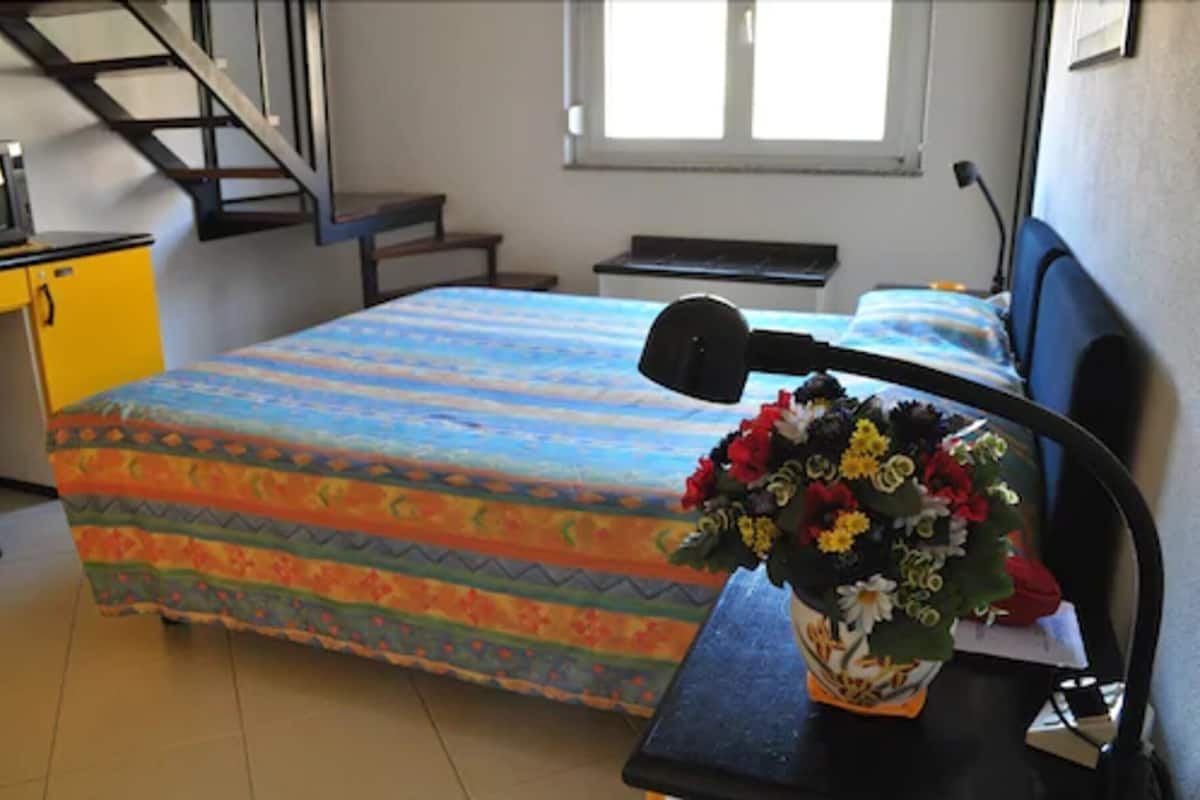 A bedroom with a bed, a desk, a chair, a window, and a staircase.
