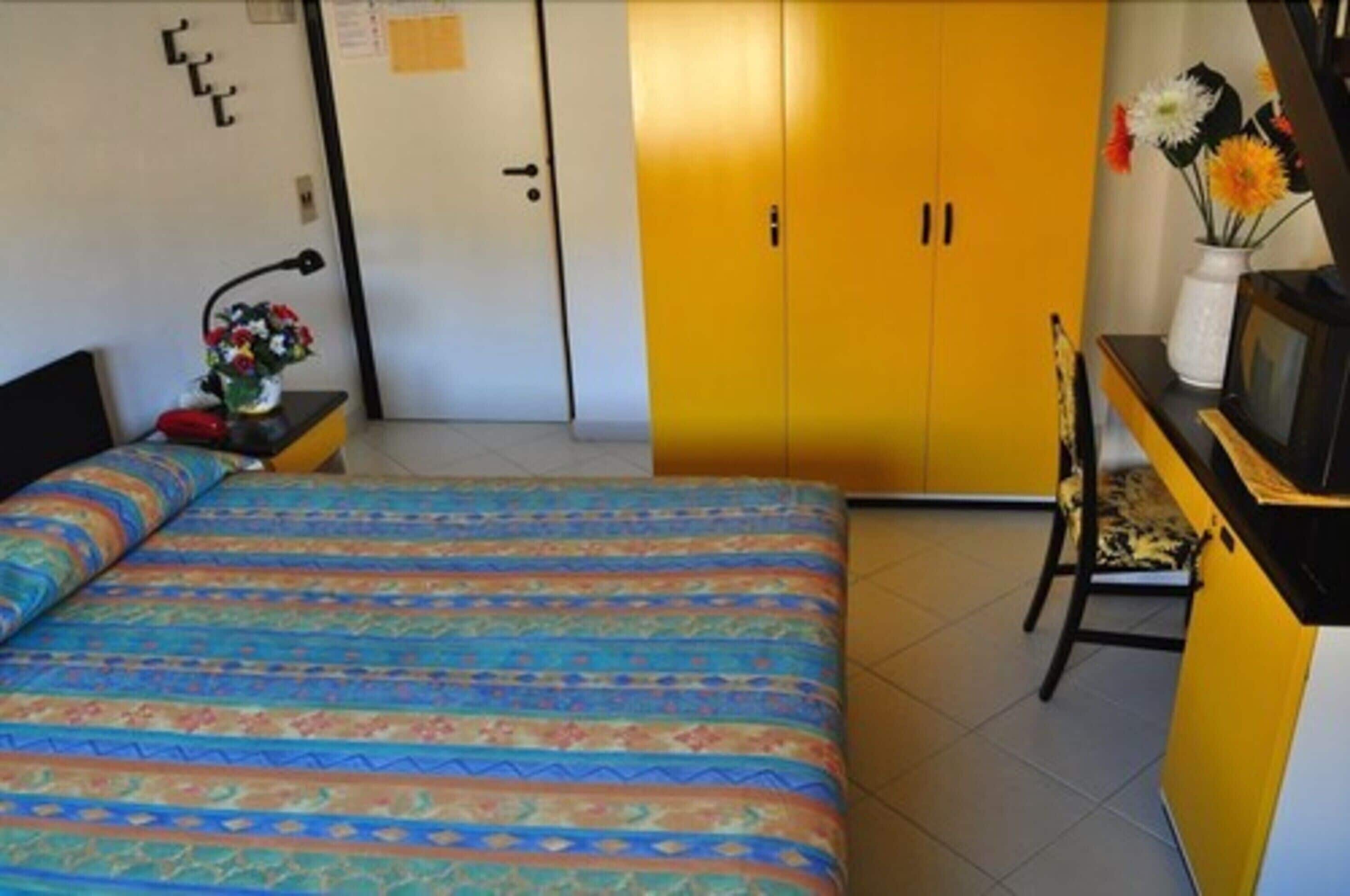 Een slaapkamer met een bed, een bureau met een computer, een stoel en een kledingkast.