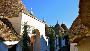 A narrow street lined with traditional buildings featuring conical roofs and white walls. - Trulli e Puglia (Alberobello)