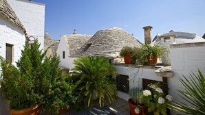 A courtyard with white buildings, stone roofs, and potted plants. - Trulli e Puglia (Alberobello)