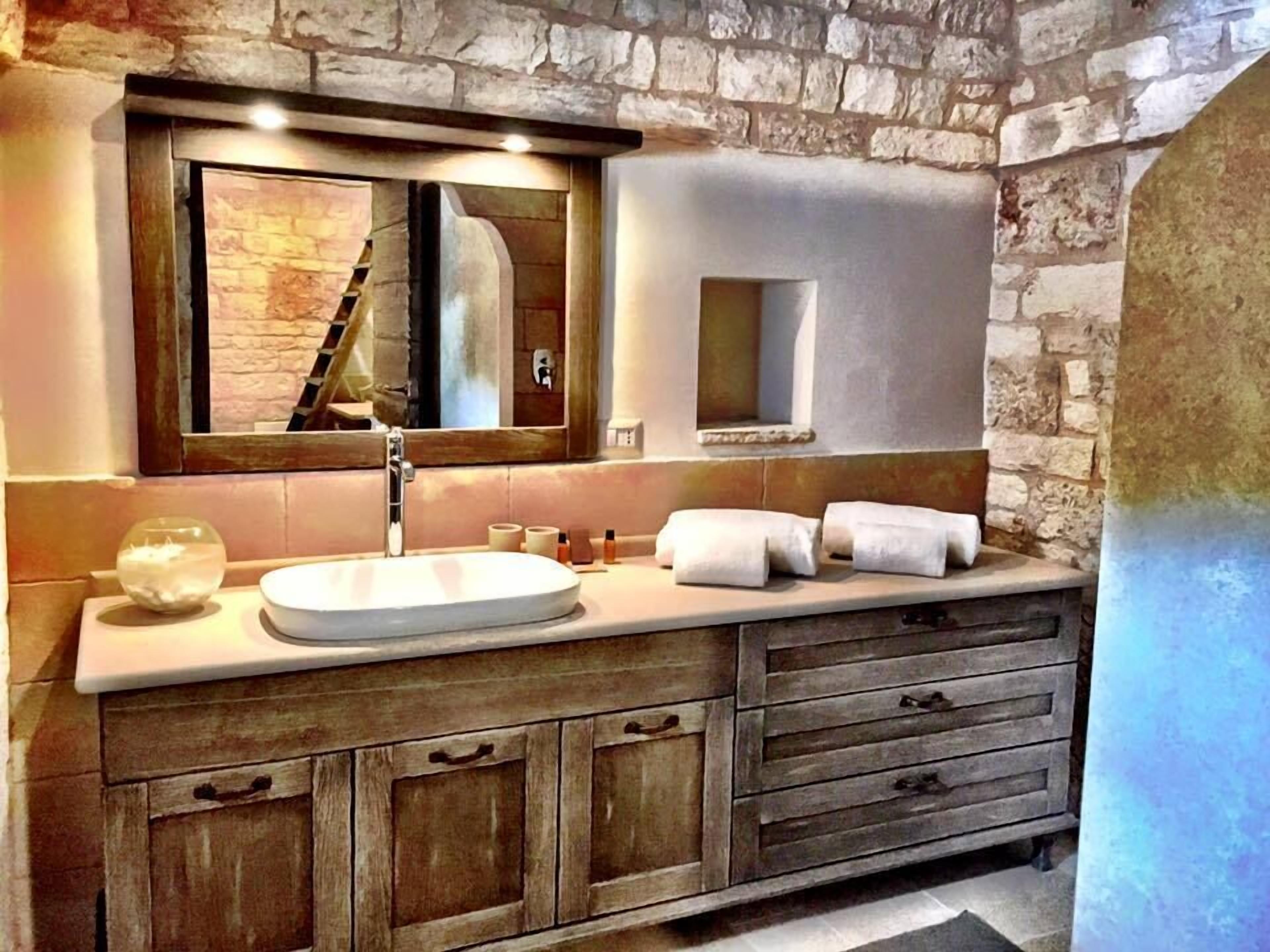 A bathroom with a stone wall, a wooden vanity, a large mirror, and a sink.