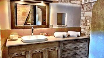 A bathroom with a stone wall, a wooden vanity, a large mirror, and a sink.