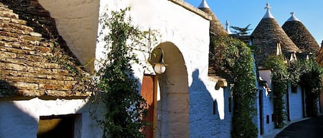A narrow street with traditional stone buildings, one with a white facade and a red door, and conical roofs.