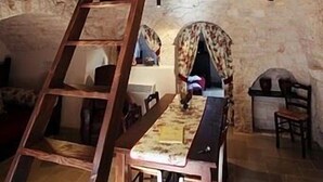 A rustic interior with a wooden staircase, a dining table, and a stone wall. - Trulli e Puglia (Alberobello)