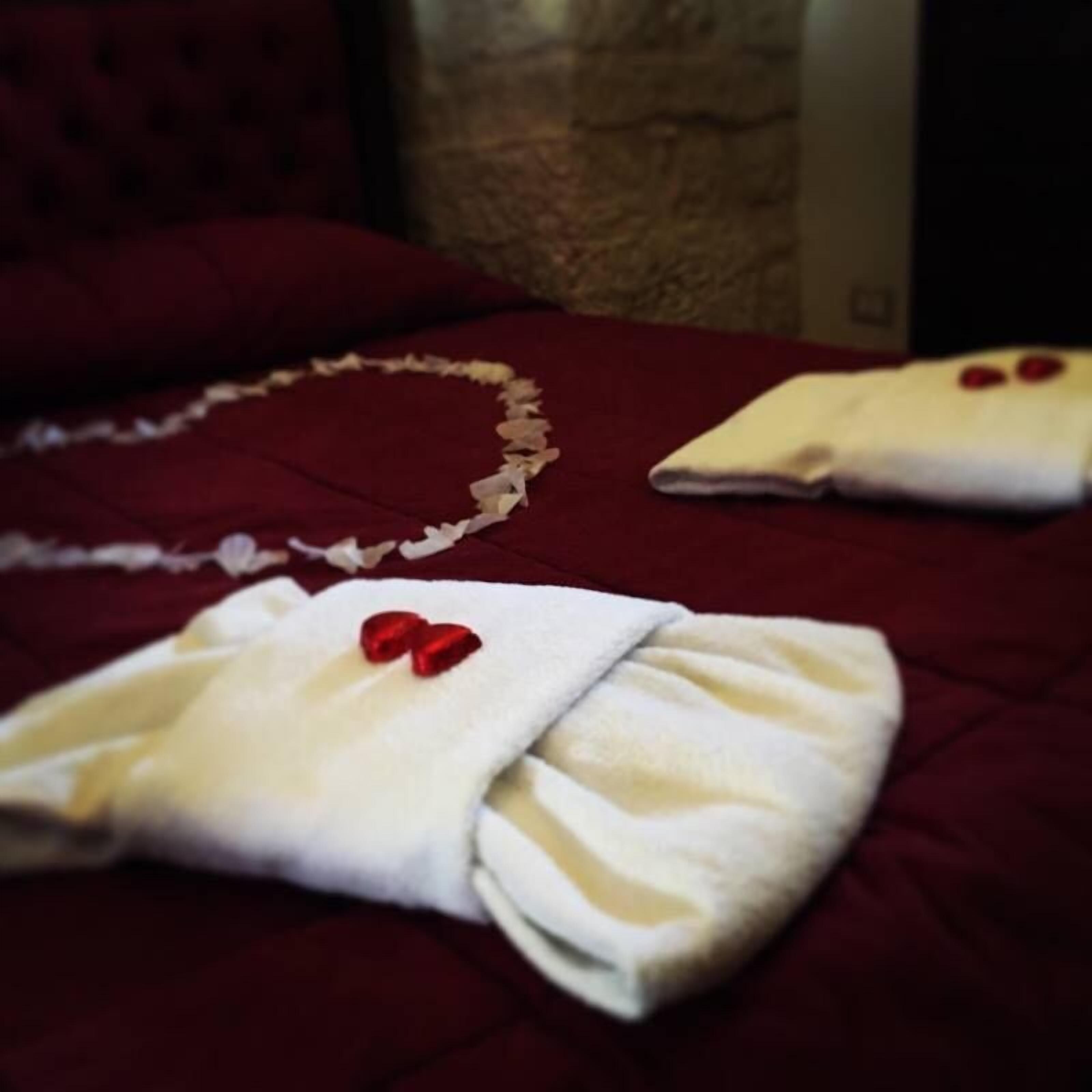 Uma cama com arranjo de pétalas de rosa em formato de coração e duas toalhas com corações vermelhos.