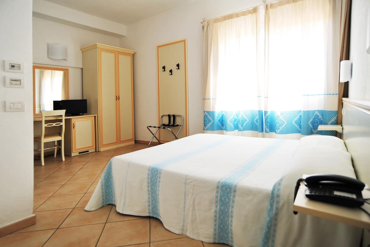 Habitación de hotel con cama, escritorio con televisor, armario y ventana con cortinas.