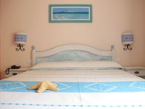 A bedroom with a bed, a starfish decoration, a painting of a beach scene, and two wall-mounted lamps. - Hotel Stella Marina (San Teodoro)