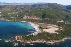 Vista aérea de una zona costera con playa, un pequeño asentamiento y terreno montañoso.