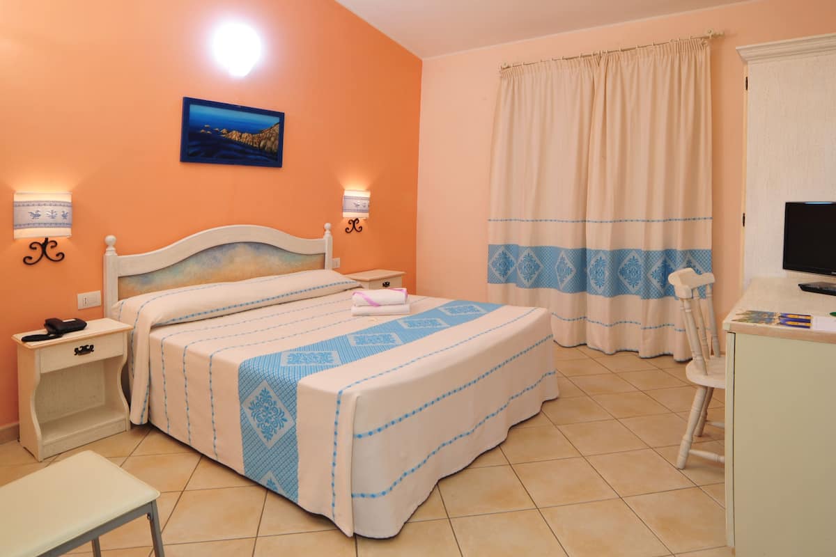 Un dormitorio con cama, mesitas de noche, escritorio, silla, televisor y ventana con cortinas.