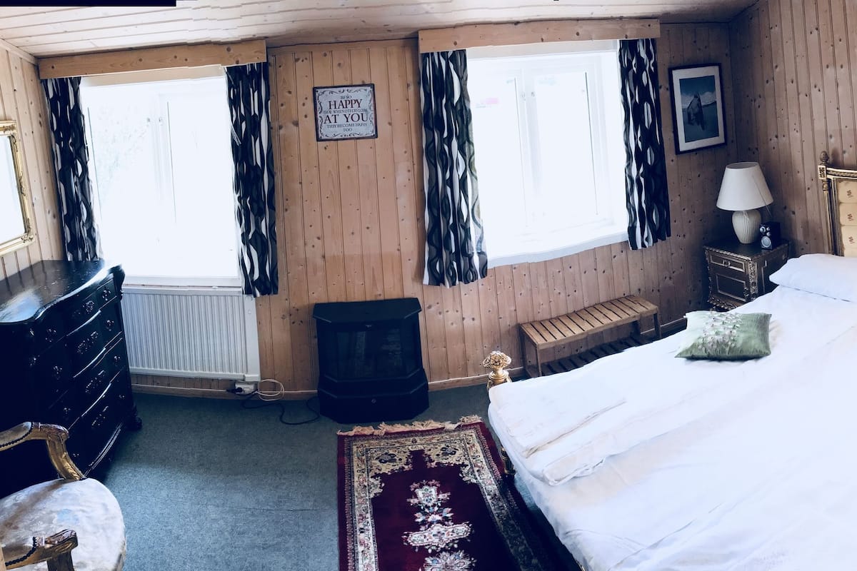 Una habitació amb un llit gran, un taulell de fusta, un mirall i una finestra amb cortines.