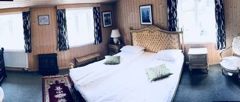 Una habitación con una cama grande, un aparador de madera, un espejo y una ventana con cortinas.