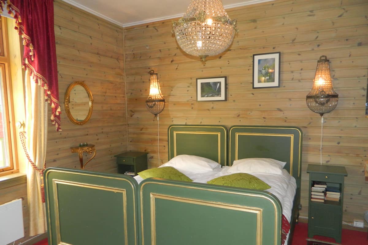 Una habitació amb un llit matrimoniàl amb cortines verdes, dues làmpades penjades a la paret, un mirall i un penjoll.