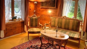A cozy room with a wooden interior, a green-striped sofa, a matching armchair, a small table, and a large window with curtains. - Eidfjord Gjestgiveri (Eidfjord)
