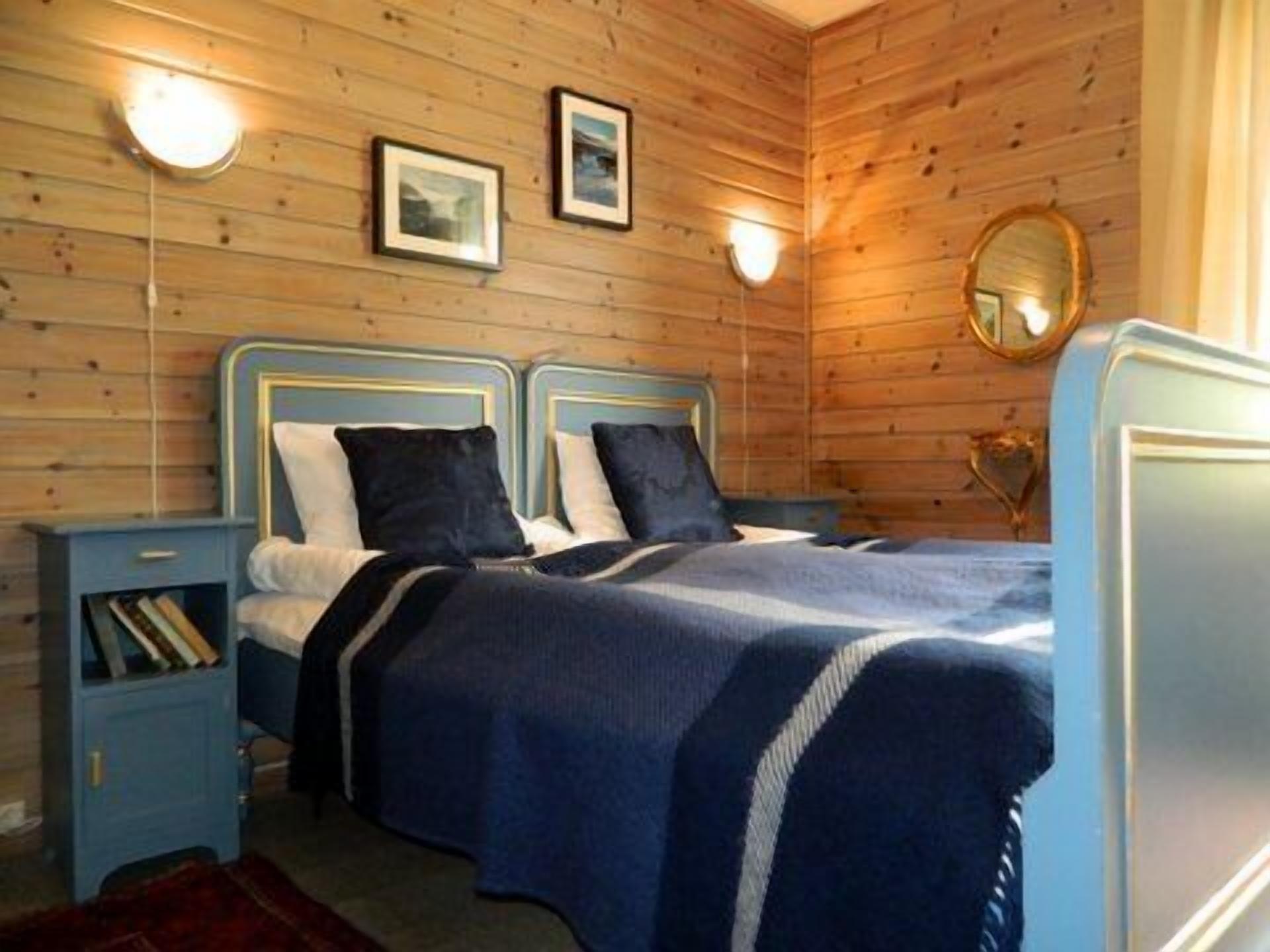 Une pièce aux murs lambrissés, comprenant deux lits, des tables de chevet et des lampes fixées au mur.