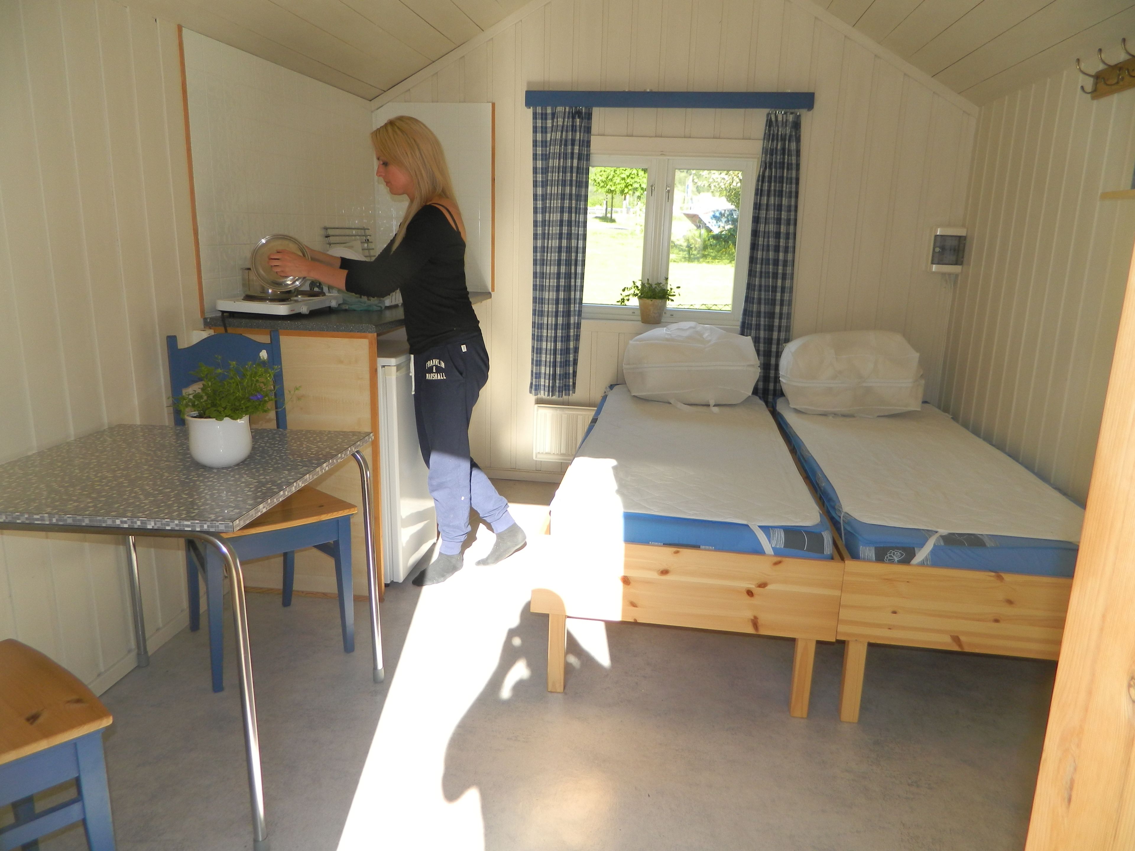 A compact room with a kitchenette, a single bed, a small table with a chair, and a window with curtains.